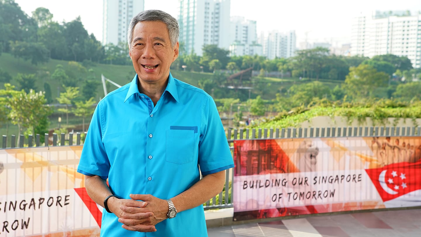 Lee Hsien Loong in a blue shirt, watch visible, hands clasped.